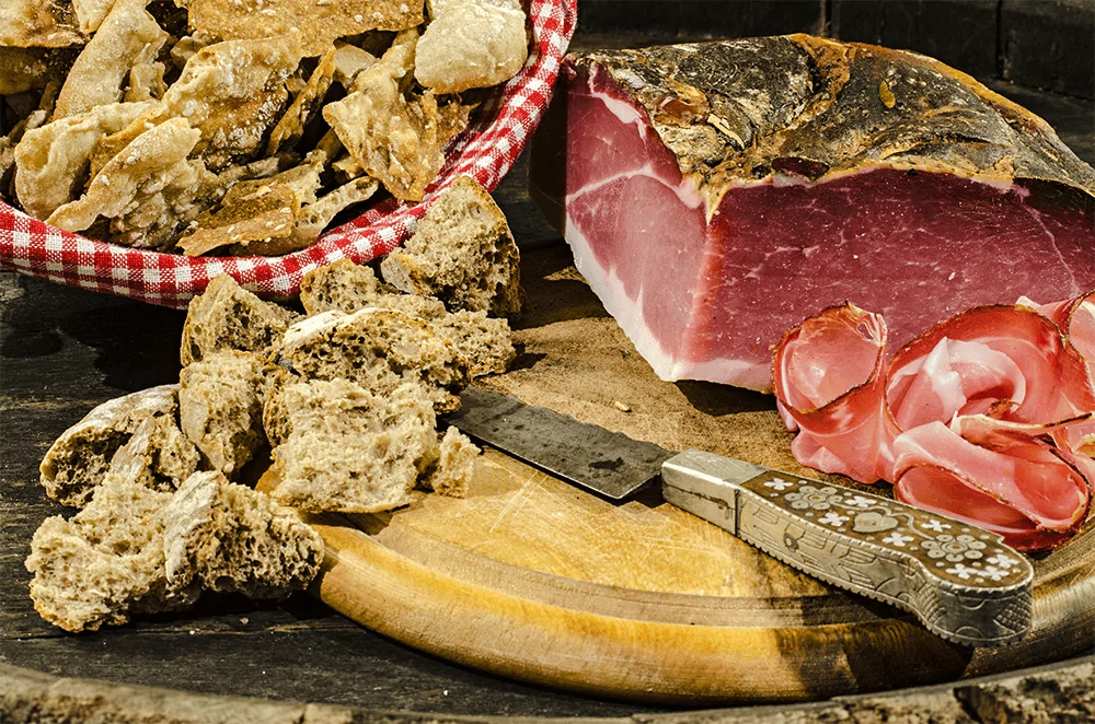 Südtiroler Speck mit Südtiroler Schüttelbrot und Grammelbrot als Brotzeit auf einem Holzbrett serviert
