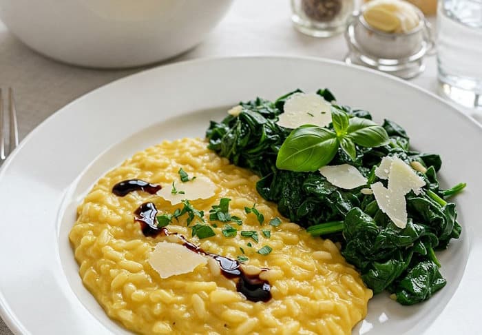 Klassischer Risotto alla Parmigiana mit Spinat und Parmesan-Raspeln garniert mit Balsamico-Creme.